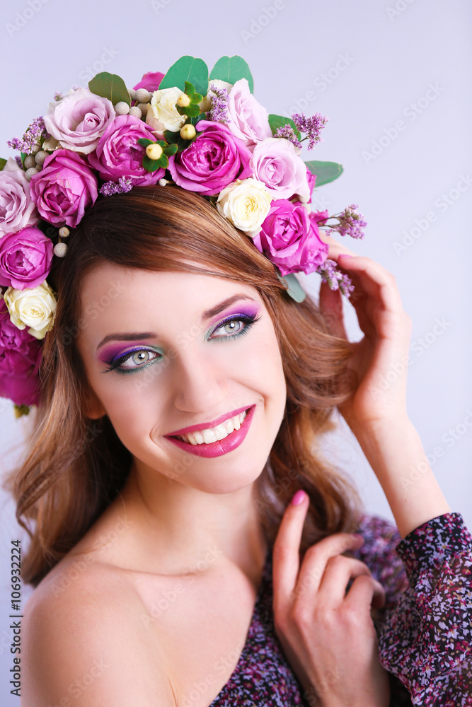 Beautiful young woman wearing floral headband on a grey background