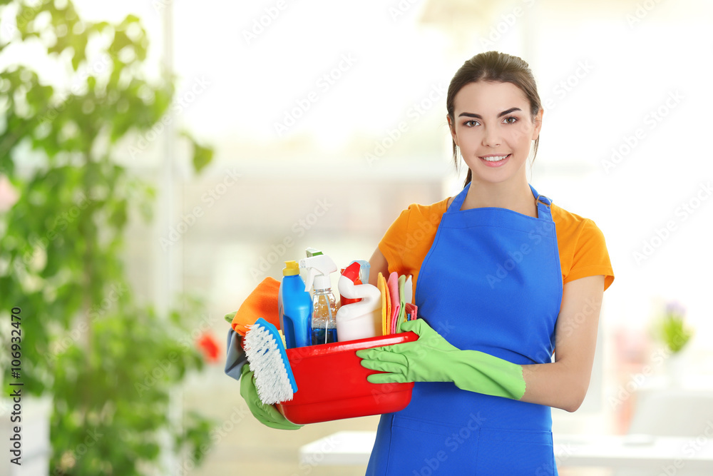Woman in rubber gloves holding basin with detergents on blurred background Woman in rubber gloves holding basin with detergents on blurred background