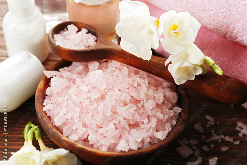 Spa composition with sea salt in a bowl, soft towels and flowers on wooden background, close up Spa composition with sea salt in a bowl, soft towels and flowers on wooden background, close up