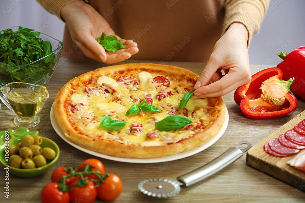 Woman decorating fresh baked pizza with basil, close up Woman decorating fresh baked pizza with basil, close up