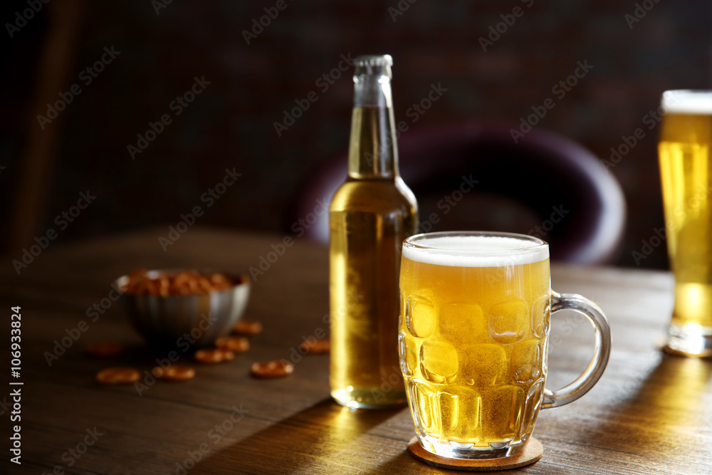 Glass mug of light beer with bottle and snacks on wooden table Glass mug of light beer with bottle and snacks on wooden table