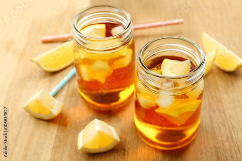 Jar of ice lemon tea with straw on wooden table