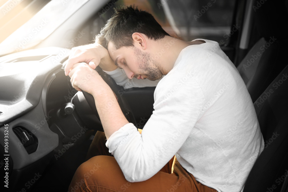 Tired young man asleep on steering wheel in his car.
