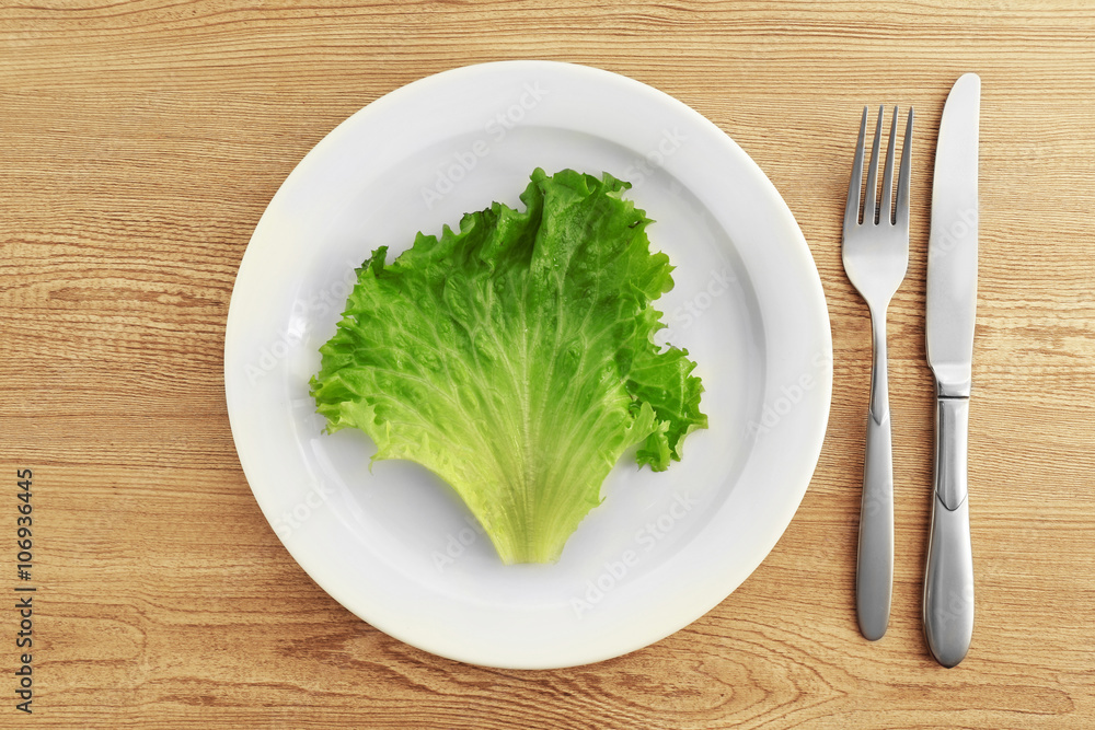White plate with salad leaf on wooden background White plate with salad leaf on wooden background