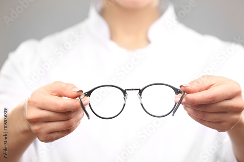Young female doctor giving glasses on grey background