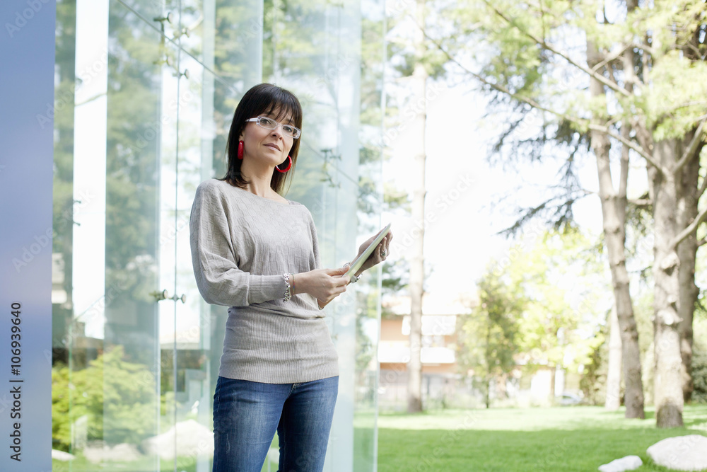 Businesswoman holding digital tablet by glass wall Businesswoman holding digital tablet by glass wall