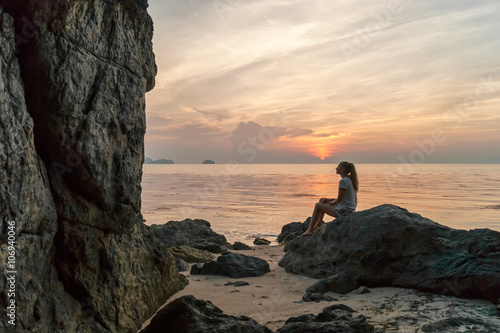 Young woman sitting on a rock watching sunset 