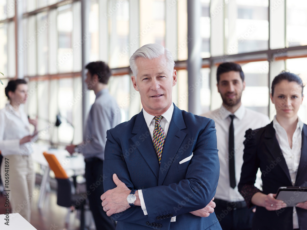 portrait of senior businessman as leader  with staff in backgrou