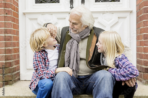 Grandfather sitting with grandchildren on front doorstep photo