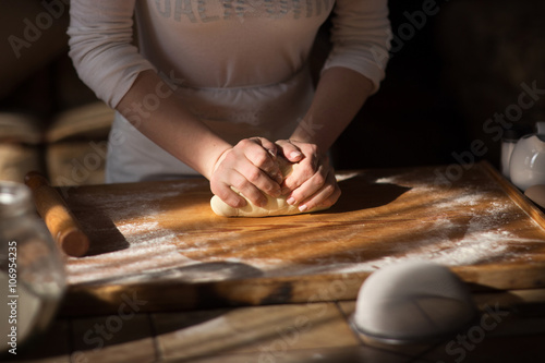 Baker hands kneading dough in flouron table