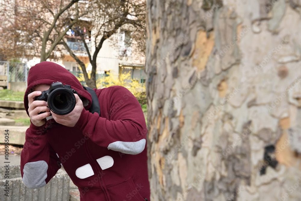 Mysterious paparazzi photographer with the hood on his head lurking behind the tree Mysterious paparazzi photographer with the hood on his head lurking behind the tree