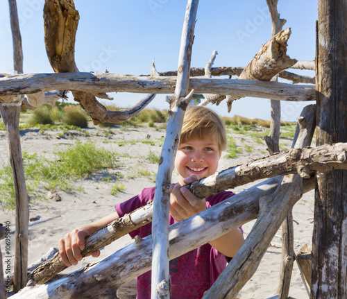 Boy placing driftwood to construct shelter, Caleri Beach, Veneto, Italy photo