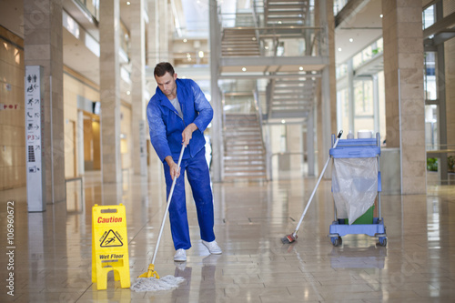 Male cleaner mopping in office atrium photo