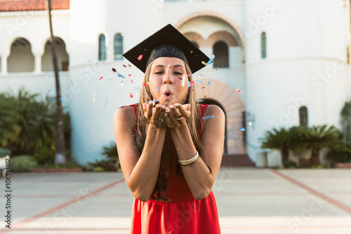 Female graduate blowing confetti from hands photo