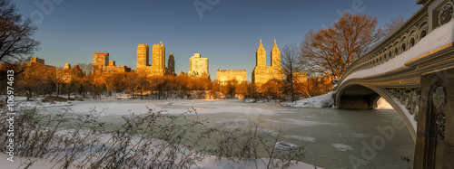 Panoramic winter sunrise on frozen Central Park Lake with Bow Bridge and view of Upper West Side buildings. Manhattan, New York City
