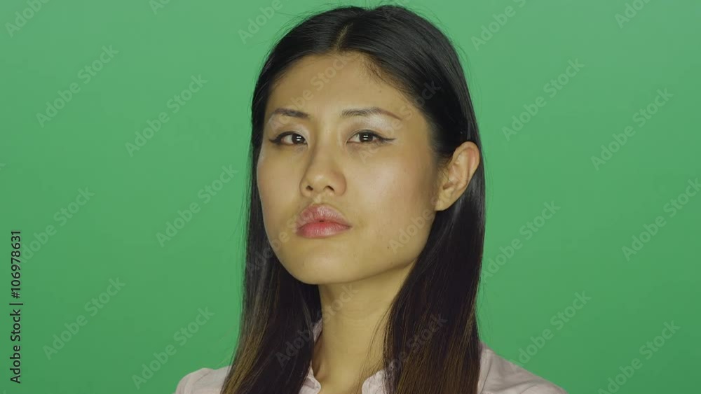 Beautiful Asian woman stares intensely with her arms closed, on a green screen studio background Beautiful Asian woman stares intensely with her arms closed, on a green screen studio background