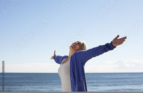 Mature woman on beach with arms outspread