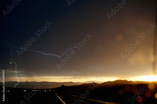 Car headlights on silhouetted highway during thunderstorm photo