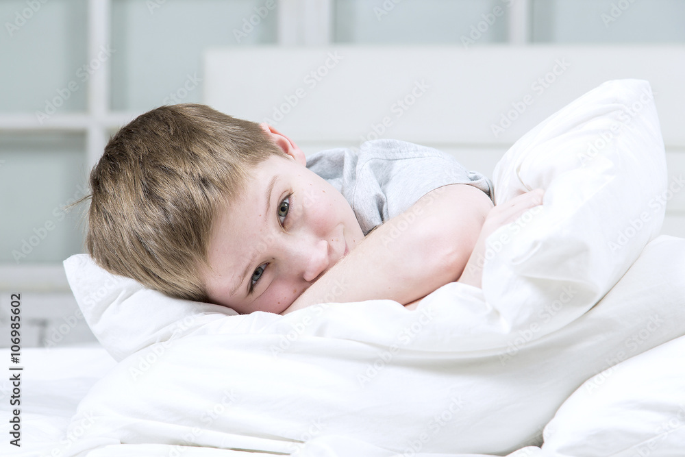 Beautiful young boy lying on the bed with white linens Beautiful young boy lying on the bed with white linens