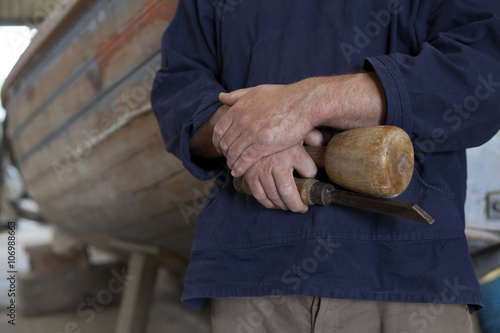 Close up of carpenters hands holding chisel in boat workshop photo