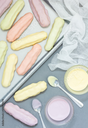 Homemade eclairs with pastel color icing on a baking sheet