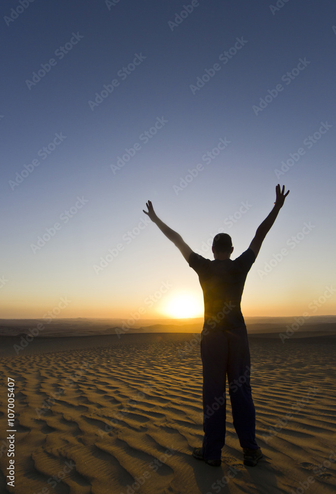 standing man with hands up at sunset in desert standing man with hands up at sunset in desert