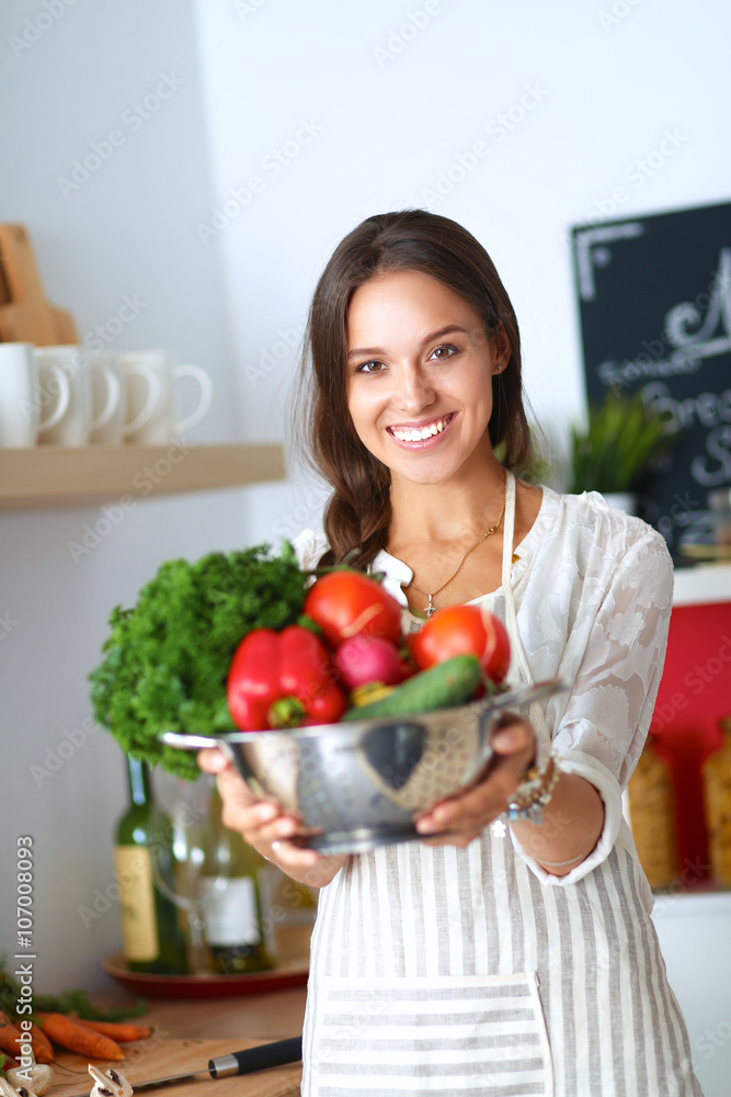 Smiling young woman holding vegetables standing in kitchen Smiling young woman holding vegetables standing in kitchen