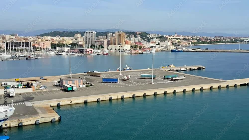 The Island of Sardinia. Panorama of The Port and The Coastal Part of The City of Cagliari From The Deck of a Cruise Ship. Sunny Day, Blue Mediterranean Sea. The Island of Sardinia. Panorama of The Port and The Coastal Part of The City of Cagliari From The Deck of a Cruise Ship. Sunny Day, Blue Mediterranean Sea.