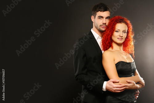 Young couple in dress and suit embracing on black background