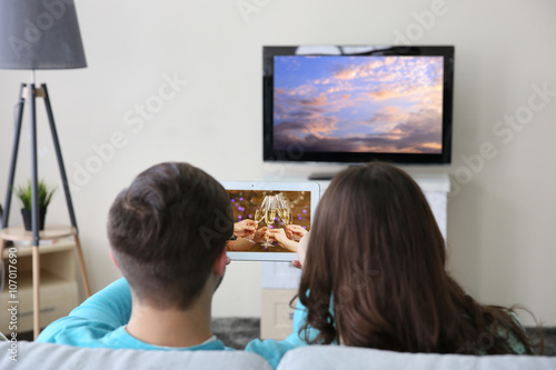 Young couple with tablet watching and taking video from the TV at home