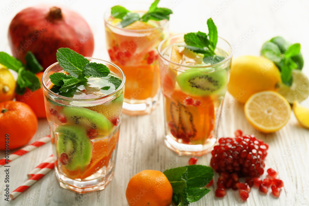 Refreshing cocktails with ice, mint, pomegranate seeds and slices of fruits on light wooden background Refreshing cocktails with ice, mint, pomegranate seeds and slices of fruits on light wooden background