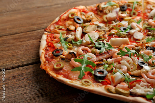 Pizza with seafood, red pepper and olives on wooden table