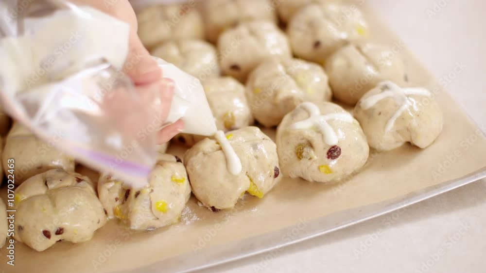 Chef pipes cross shapes with flour paste on to hot cross bun dough balls on a baking sheet in preparation for baking. Slow motion, originally recorded in 4K at 60fps. Chef pipes cross shapes with flour paste on to hot cross bun dough balls on a baking sheet in preparation for baking. Slow motion, originally recorded in 4K at 60fps.