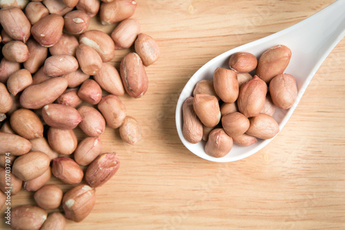 spoon of peanut and a pile peanut on a wooden background.