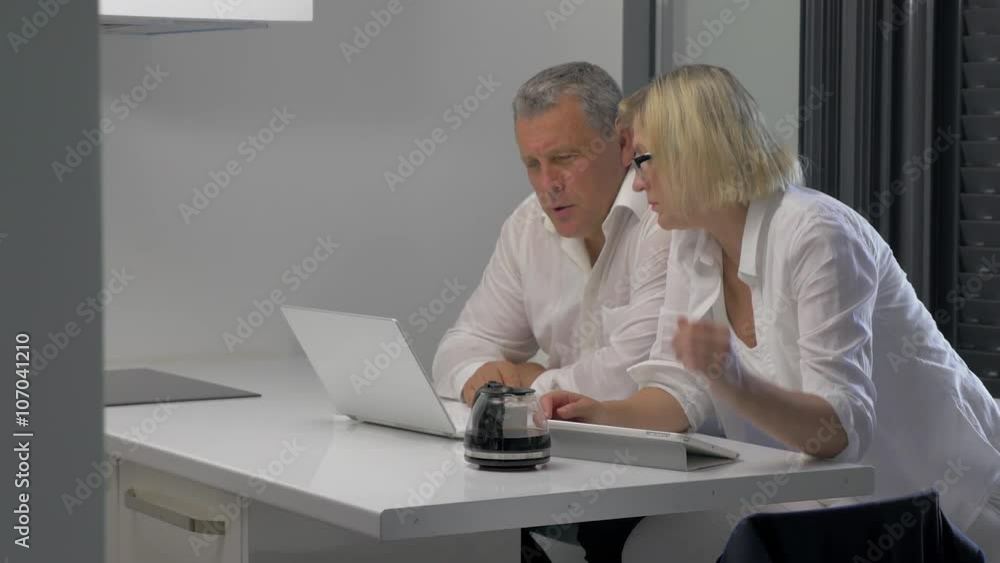 Mature man and woman with laptop and tablet PC working on business indoor. They drinking coffee when doing job Mature man and woman with laptop and tablet PC working on business indoor. They drinking coffee when doing job