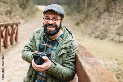 Young man bearded with film photocamera in the forest