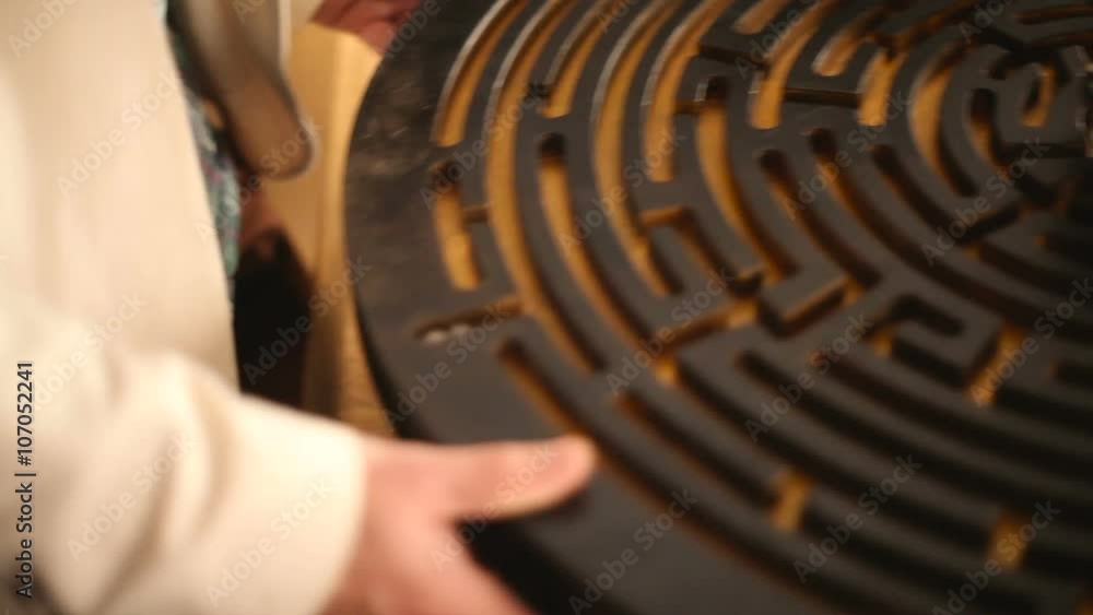 the hands of a human player trying to find a way for a small round ball in a wooden maze the hands of a human player trying to find a way for a small round ball in a wooden maze