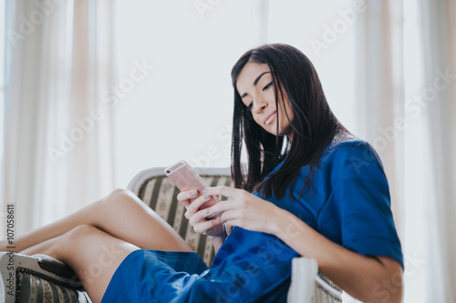 Portrait of cute teen girl texting emotional in a white bright room, spring sunny day