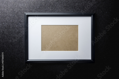Black plain empty thin wood picture frame with white mat passe-partout on black rough paint wall background
