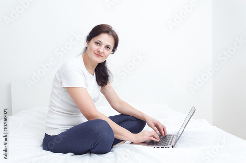 similg happy woman sit in bed with a laptop working from home photo