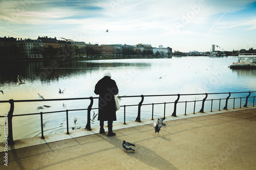 Canvas Print an old woman feeding the birds on river bridge: vintage colors preset
