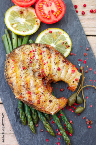A sturgeon steak served with asparagus, lemon, tomatoes, capers and spices