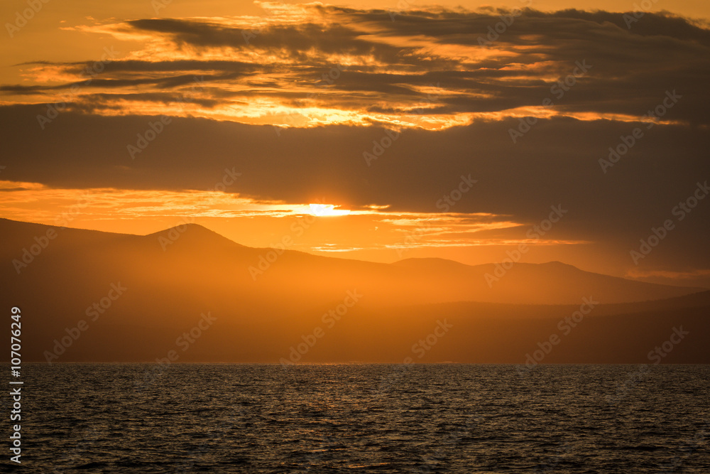 Orange dawn over hilly coastline and ocean