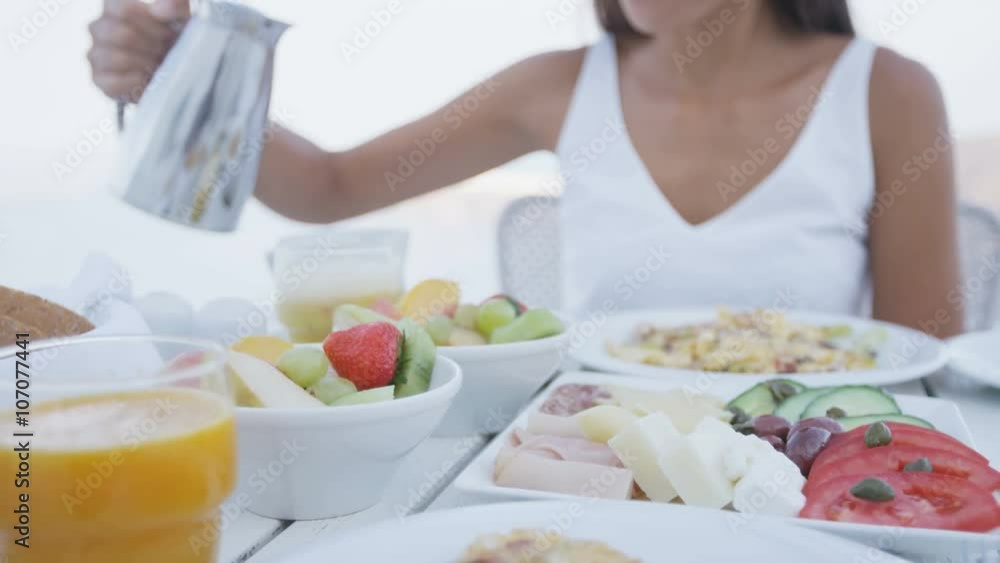 Young woman pouring coffee into cup. Variety of healthy food is served on terrace resort. Female is having delicious breakfast on vacation. Young woman pouring coffee into cup. Variety of healthy food is served on terrace resort. Female is having delicious breakfast on vacation.
