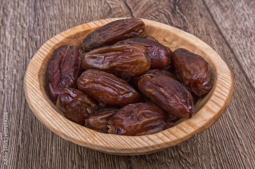 Dried dates in a wooden bowl on a wooden background