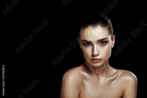 Beauty Portrait of Young Woman with Strobing Makeup Liquid on Face. Wet Body Effect. Strobing Highlighting technique. Professional Retouch. Studio Photo. Ideal commercial concept. Black background