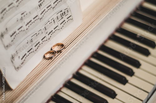 Pair golden rings on classic, piano keyboard with music notes. Wedding accessories. Black and white background, selective focus 