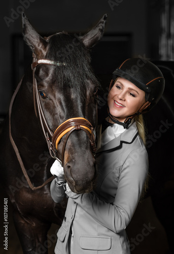 Fototapeta Naklejka Na Ścianę i Meble -  Horsewoman in uniform with a brown horse in the stable.