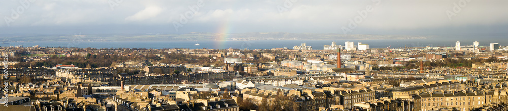 Wide panorama of Edinburgh with a little rainbow; in the background the water of the Firth of Forth, and behind it, on the opposite shore, county Fife.