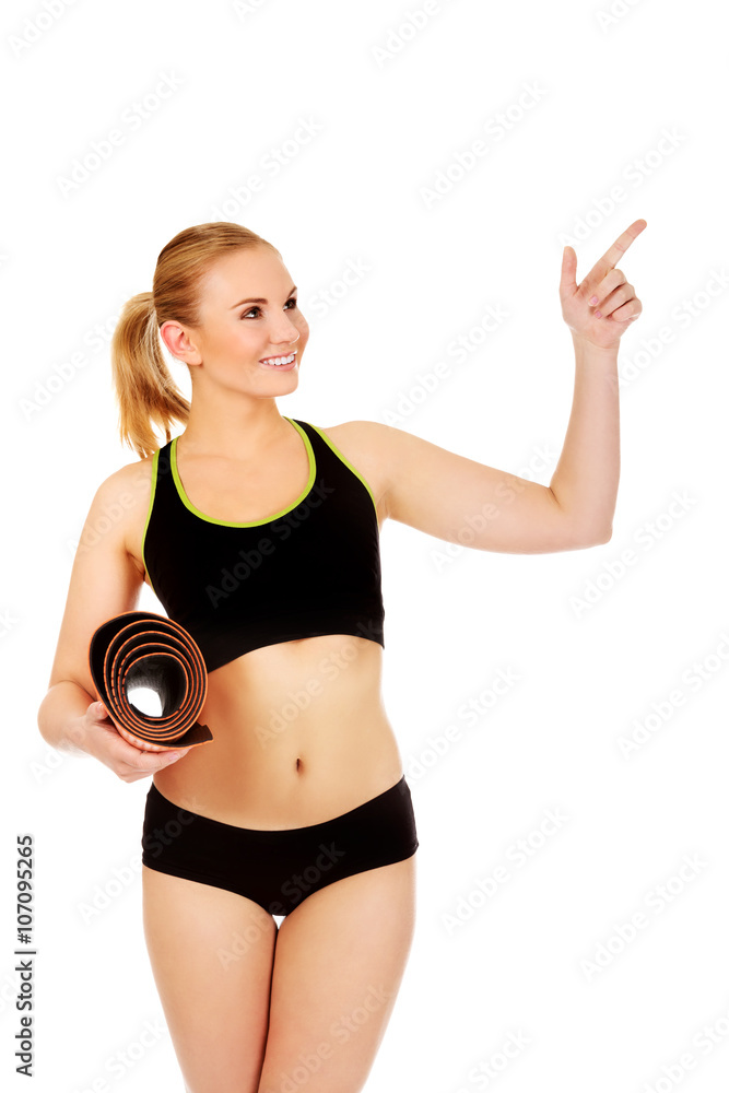 Young athletic woman holding mat and pointing for something Young athletic woman holding mat and pointing for something